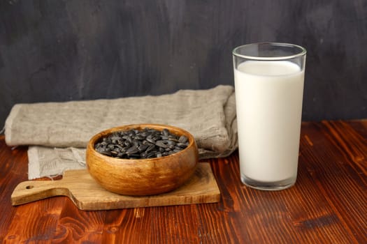 Sunflower milk in a glass, raw seeds,wooden background. Dairy free alternative