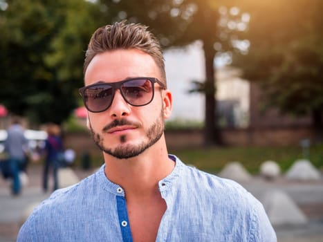 One handsome young man in urban setting, standing, wearing shirt and sunglasses looking at camera