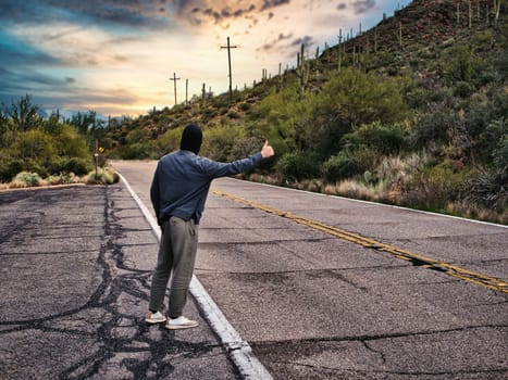 Back of young man, a hitchhiker waiting for car on roadside in city, wearing hoodie sweater in Arizona, USA