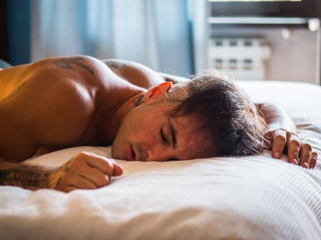 Handsome shirtless young man sleeping in bed on blue pillow, with peaceful expression