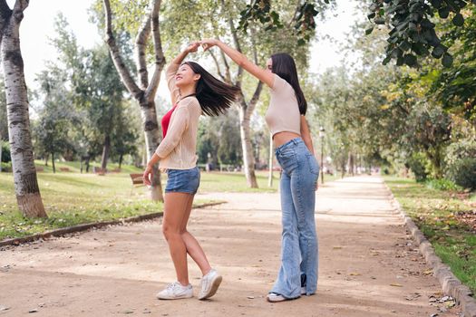 couple of happy women dancing and having fun during a date in a park, concept of friendship and love between people of the same sex