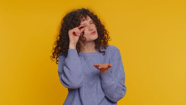 Need some more, please give me. Curly haired woman showing a little bit gesture with sceptic smile, showing minimum sign, measuring small size. Young girl isolated alone on yellow studio background
