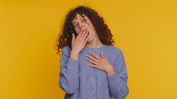 Tired curly haired woman yawning, sleepy inattentive feeling somnolent lazy bored overworked gaping suffering from lack of sleep. Young exhausted teen girl isolated alone on yellow studio background