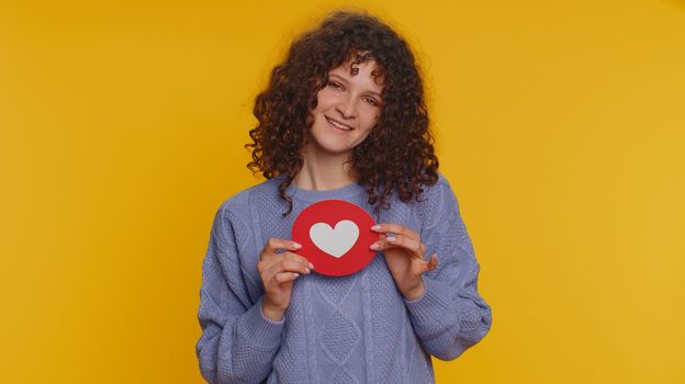 Like. Hipster curly haired woman show heart banner inscription agrees with something, gives positive reply recommends advertisement likes good. Young girl isolated alone on yellow studio background