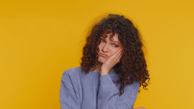 Sad curly haired woman tired bored indifferent expression, exhausted of tedious story, not interested in communication talk, displeasure, uninteresting. Young girl isolated on yellow studio background