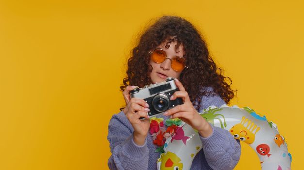 Happy young woman tourist photographer in sunglasses taking pictures photos on retro camera. Travel, summer holiday vacation, trip to seaside. Teen smiling girl traveler on studio yellow background