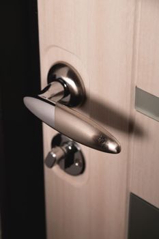 Close up, stylish new metal doorknob on modern interior door. Shiny silver doorknob on a light door. The concept of interior details.