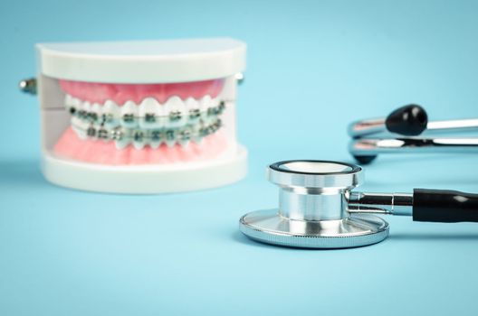 Medicine equipment stethoscope and metal wire dental braces on model teeth on blue background. Health dental care concept.
