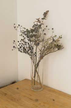 Dry plants in minimalistic glass jar. Vertical image of branch with dry leaves in stylish simple glass vase. Decoration and interior