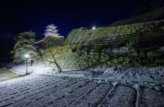 Japanese castle towers over stone wall and snow-covered steps on winter night. High quality photo