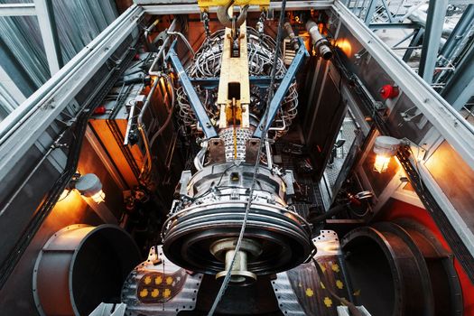 The engine of a gas turbine compressor hangs on a crane during installation in a module for generating electricity