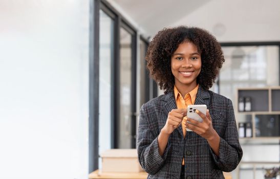 Portrait of elegant successful asian business woman speaking by smartphone and smiling happily while standing against window in office