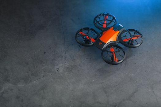 Orange quadcopter mini spy drone on a dark background with blue backlight and free space