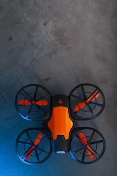 Orange quadcopter mini spy drone on a dark background with blue backlight and free space