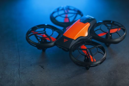Orange quadcopter mini spy drone on a dark background with blue backlight and free space