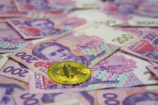 Golden bitcoin on two hundred ukrainian hryvnia bills background. Ukrainian grivna to Bitcoin concept