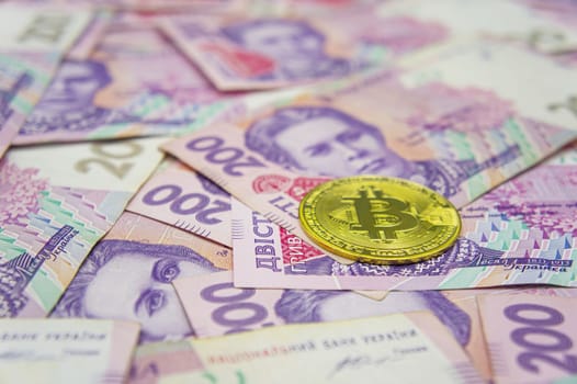 Golden bitcoin on two hundred ukrainian hryvnia bills background. Ukrainian grivna to Bitcoin concept