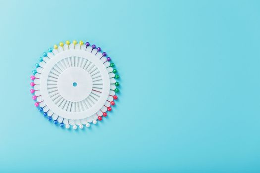 A set of multicolored needles pins in a round platform on a blue background with free space