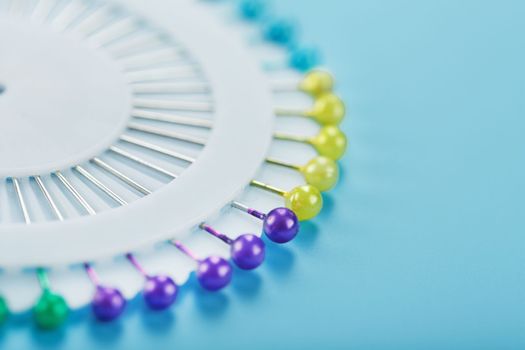 A set of multicolored needles pins in a round platform on a blue background with free space