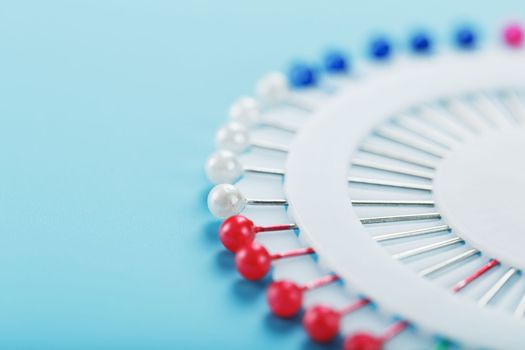 A set of multicolored needles pins in a round platform on a blue background with free space