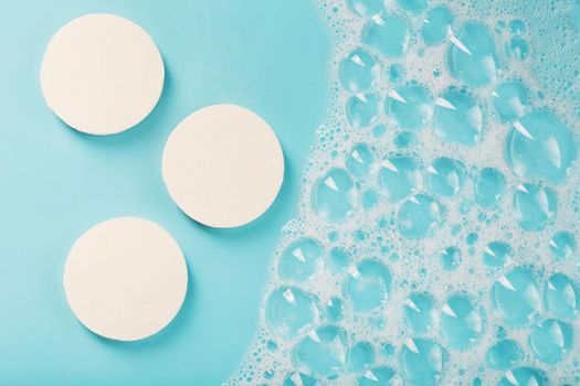 Three bars of round soap with foam on a blue background