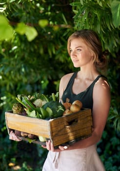 Shes down to earth. A young woman holding a crate of vegetables outdoors