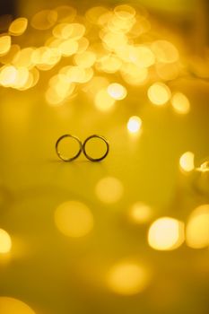 Wedding rings on blured bokeh glowing golden background. Symbol of love and romance on a textured glitter background with copy space for your greeting or congratulations.
