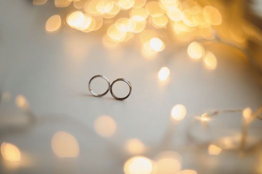 Wedding rings on blured bokeh glowing golden background. Symbol of love and romance on a textured glitter background with copy space for your greeting or congratulations.