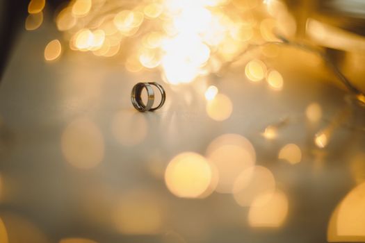 Wedding rings on blured bokeh glowing golden background. Symbol of love and romance on a textured glitter background with copy space for your greeting or congratulations.