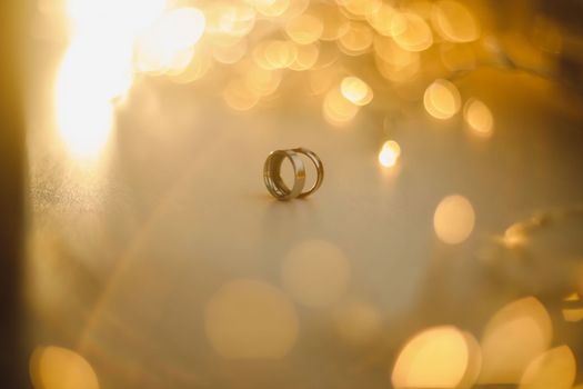 Wedding rings on blured bokeh glowing golden background. Symbol of love and romance on a textured glitter background with copy space for your greeting or congratulations.