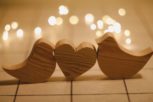 two wooden birds and heart made by bokeh lights background. Valentines day, Easter, Wedding card with wooden figures of birds, home decor.