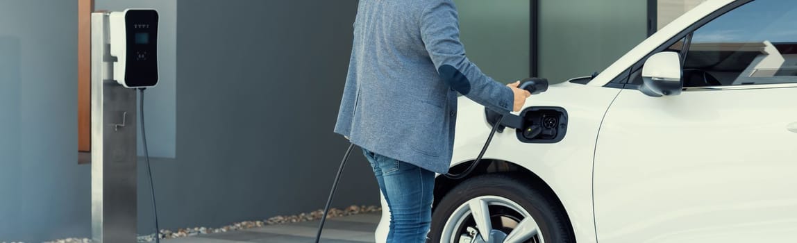 Closeup progressive asian man install cable plug to his electric car with home charging station. Concept of the use of electric vehicles in a progressive lifestyle contributes to clean environment.