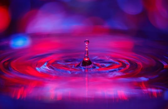 A transparent drop with a red-violet background falls into the water. Abstract colorful background