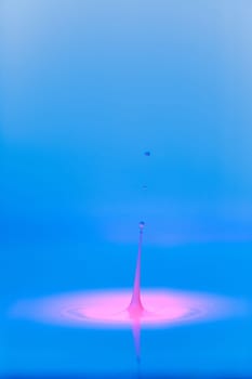 A drop falls into a thick liquid with a blue-pink background. Abstract colorful background