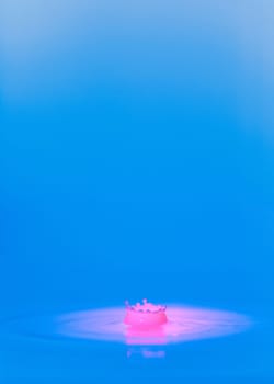 A drop falls into a thick liquid with a blue-pink background. Abstract colorful background