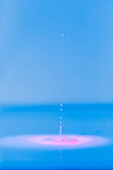 A drop falls into a thick liquid with a blue-pink background. Abstract colorful background