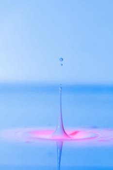 A drop falls into a thick liquid with a blue-pink background. Abstract colorful background