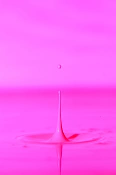 A drop falls into a thick liquid with a pink background. Abstract colorful background