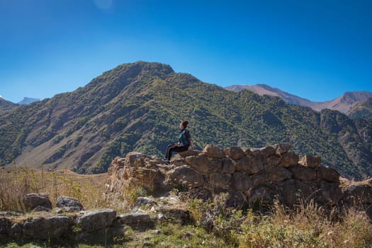 The girl sits high in the mountains on a stone and admires the views of nature