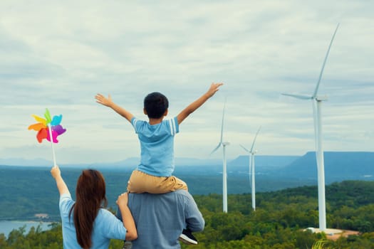 Progressive happy family enjoying their time at wind farm for green energy production concept. Wind turbine generators provide clean renewable energy for eco-friendly purposes.