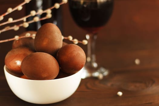 painted eggs on a plate with willow twig and a bottle of red wine on a wooden table. Easter celebration. copy space