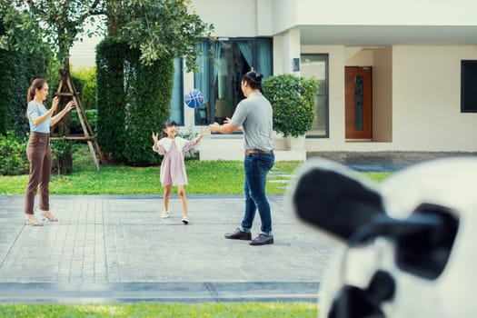 Progressive young happy family with electric vehicle and home backyard charging station. Green and clean energy from electric vehicles for healthy environment. Eco power from renewable source.