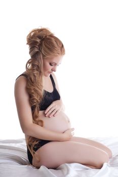 young pregnant woman sit in black lingerie in silk bed