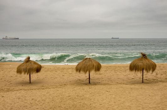 Three palm umbrellas on an empty beach in Valparaiso Chile on a cold summer day