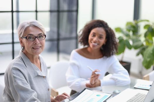 Business women smile while working together on a laptop at a table in the boardroom in the office