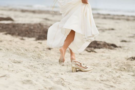Bride in white dress and golden shoes on the sandy beach