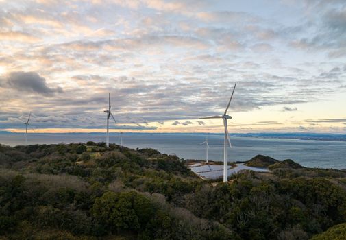 Wind Turbines Over Small Solar Farm in Green Landscape by Sea at Sunset. High quality photo