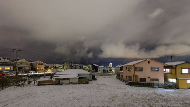 Suburban houses by snow covered field under storm clouds on winter night. High quality photo