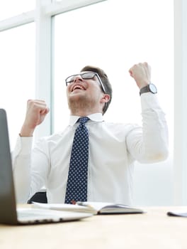 Happy young businessman raising hands in front of laptop