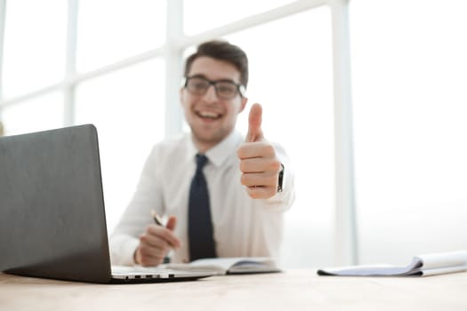 Cheerful young businessman standing and showing thumbs up in office